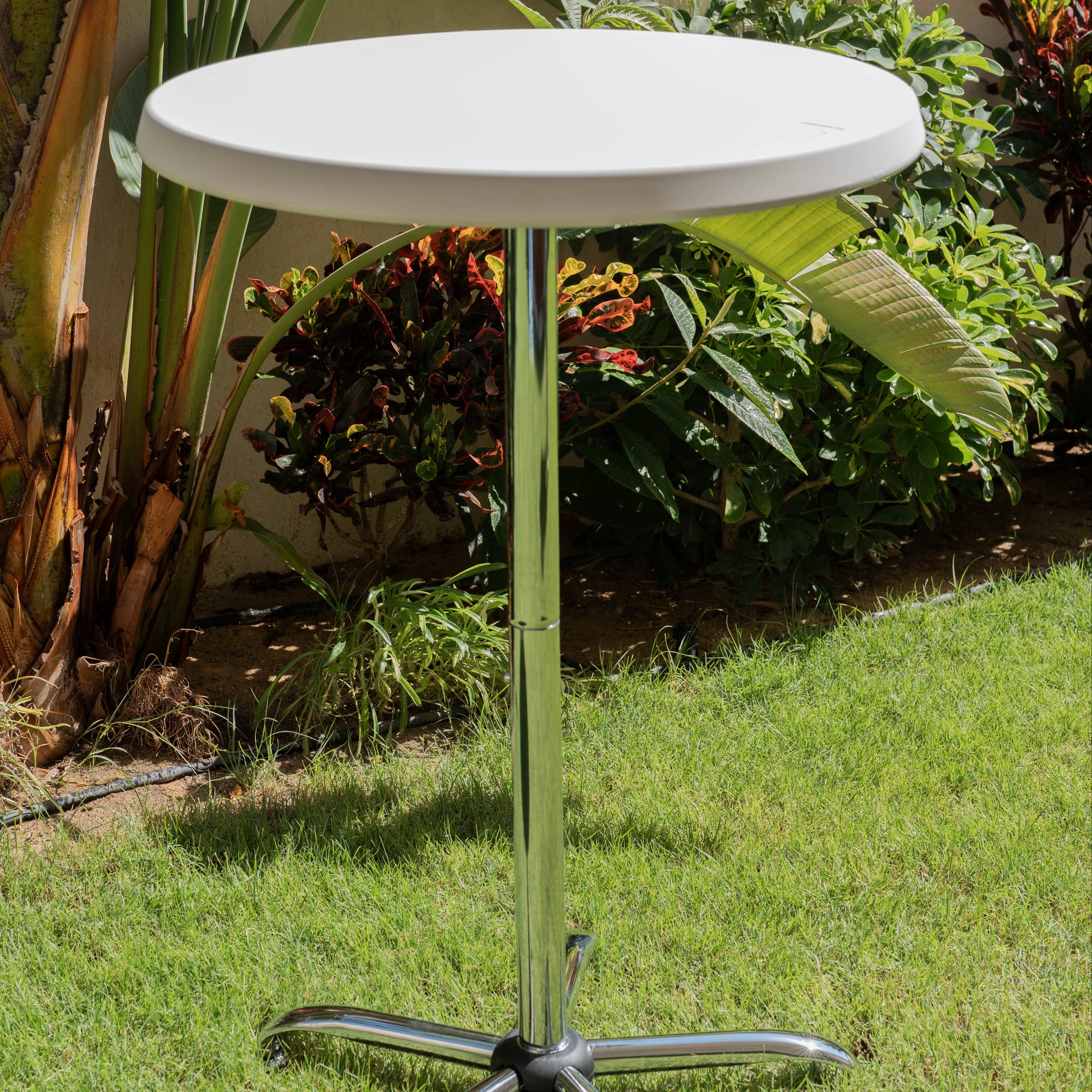 White round table with a metal base on grass with plants in the background