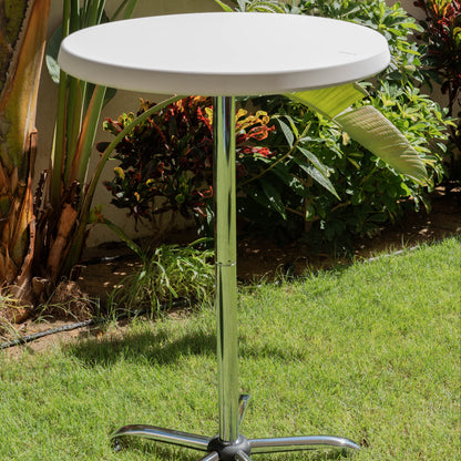 White round table with a metal base on grass with plants in the background